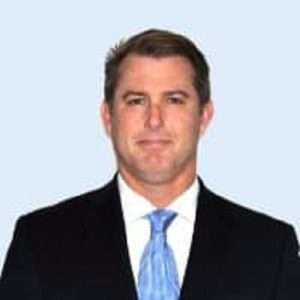 Professional portrait of John Stokoe, author and contributor to Business Booster Today, wearing a suit and tie against a light blue background.