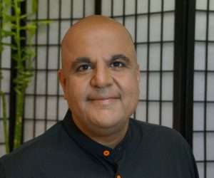 Vikas Malkani, author and entrepreneur, smiling in a professional setting with bamboo plants in the background, representing expertise in business and coaching.